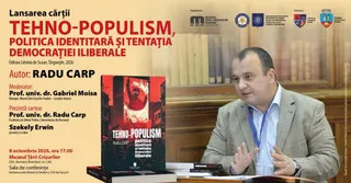 Un bărbat într-un sacou gri și cămașă albastră stă la o masă lângă o carte cu copertă neagră și roșie pe un fundal de bibliotecă.
