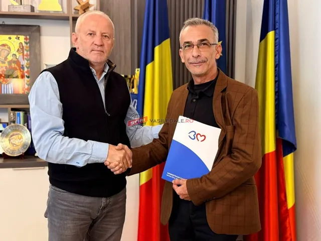 Un bărbat cu vestă neagră strânge mâna unui bărbat cu sacou maro care ține un dosar albastru și alb.