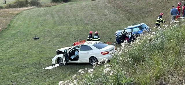 Două autoturisme sunt situate pe o panta de iarbă, în prezența unor persoane purtând echipamente de protecție colorate.