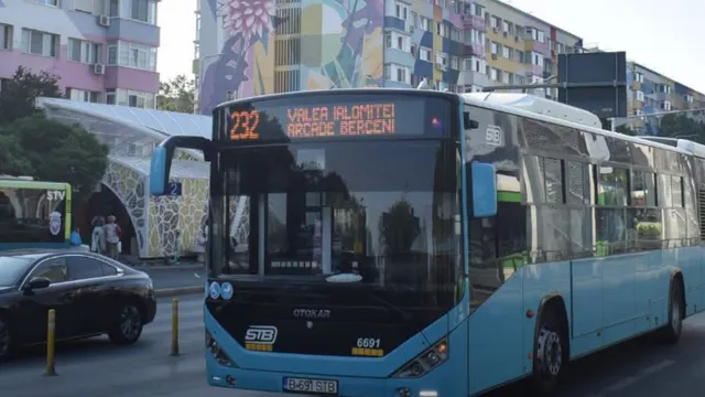 Un autobuz albastru cu numărul 232 este parcat pe un drum lângă o mașină neagră și clădiri rezidențiale colorate.