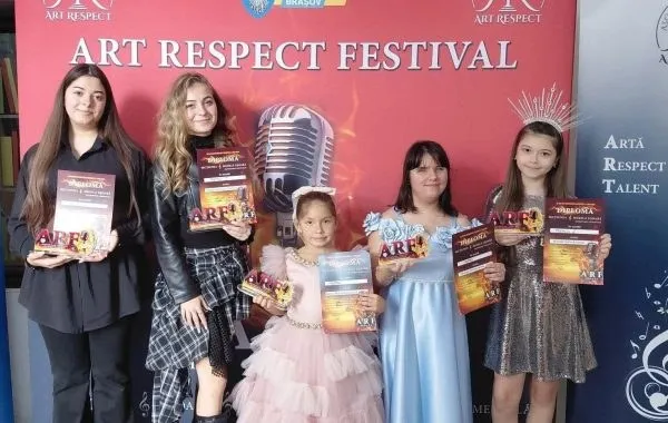 Cinci femei stau în picioare în fața unui panou roșu, fiecare ținând în mâini diplome și trofee mici.