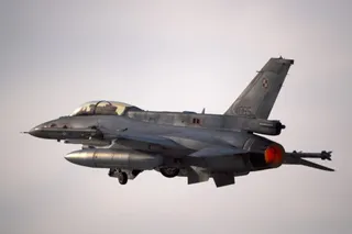 Un avion de luptă gri zboară pe cerul înzăpezit, având un motor aprins în partea din spate.