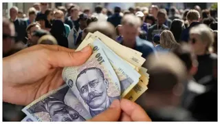 O persoană ține un teanc de bancnote în mâini, în fața unei mulțimi de oameni neclar de identificați.