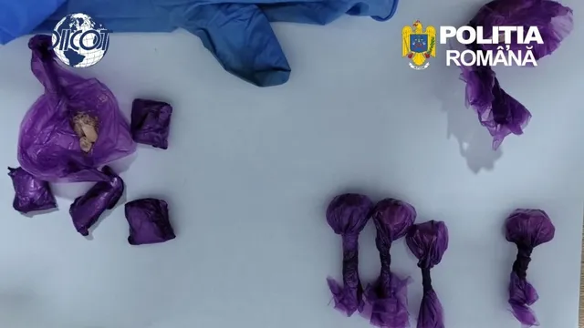 Mai multe obiecte mici învelite în pungi de plastic mov sunt așezate pe o suprafață albă lângă un material textil albastru.