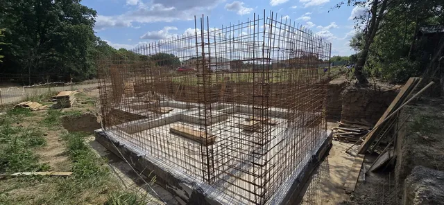 O structură de armătură metalică este instalată pe o fundație de beton într-un șantier de construcții aflat în aer liber.