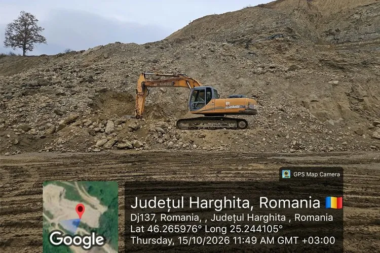 O excavatoare portocalie lucrează într-o zonă de exploatare de nisip și pietriș într-un teren accidentat sub un cer înnorat.