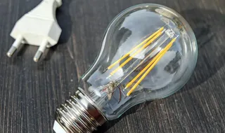 Un bec cu filament de tip LED este așezat pe o suprafață închisă lângă un cablu cu un conector alb.