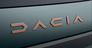 Logoul brandului Dacia este afișat pe o suprafață metalică de culoare închisă.