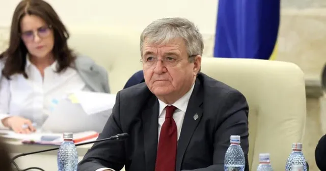 Un bărbat cu ochelari și cravată roșie stă la o masă lângă o femeie cu ochelari și sticle de apă din plastic.