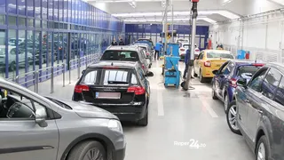 Mai multe mașini sunt parcate într-un atelier de service auto cu lifturi hidraulice și echipamente de lucru pe fundalul unor pereți albi.