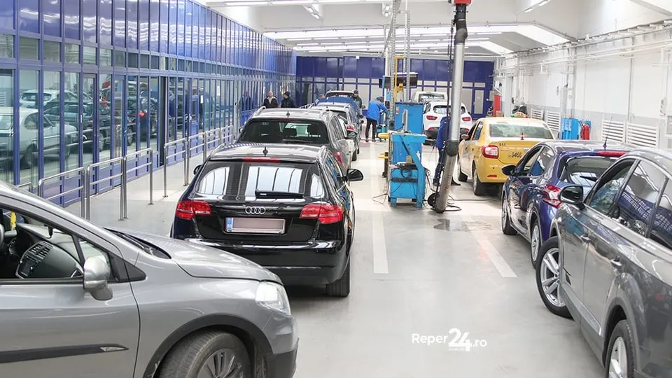 Mai multe mașini sunt parcate într-un atelier de service auto cu lifturi hidraulice și echipamente de lucru pe fundalul unor pereți albi.