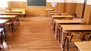 O sală de clasă cu rânduri de bănci din lemn și scaune dispuse pe un podea de parchet.