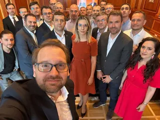 Un grup de persoane posedă pentru o fotografie de tip selfie într-o încăpere cu pereți din lemn.