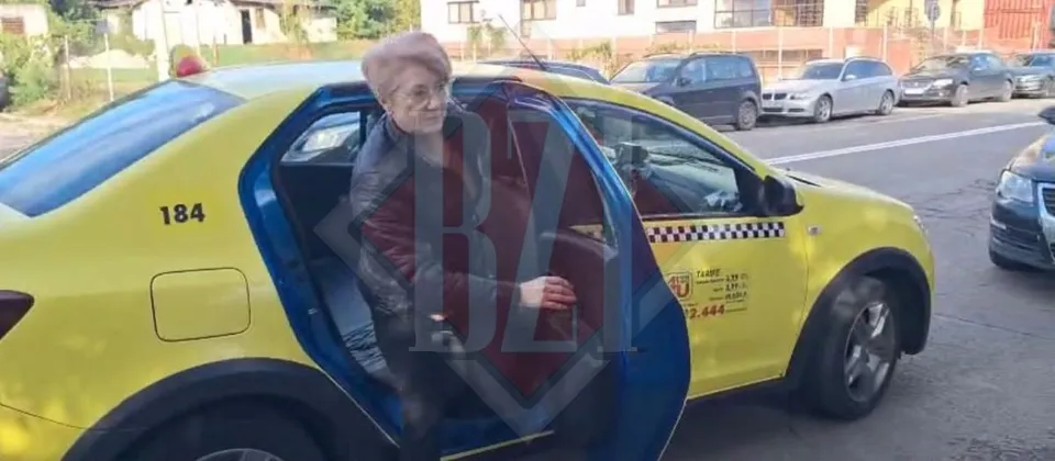 O femeie cu păr scurt și roșu coboară dintr-un taxi galben cu portierele deschise pe un drum asfaltat.