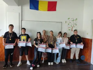 Un grup de șapte copii stă în rând în fața unei table albe, ținând diplome și purtând medalii pe gât.