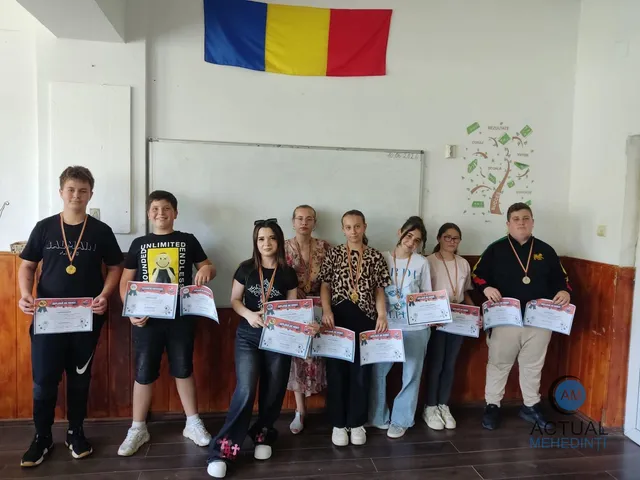 Un grup de șapte copii stă în rând în fața unei table albe, ținând diplome și purtând medalii pe gât.