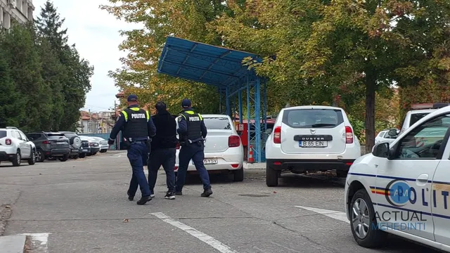Trei polițiști în uniformă întunecată merg pe un drum asfaltat printre mașini parcate și un autobuz sub un acoperiș albastru.