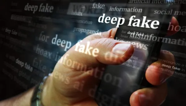 O mână ține un smartphone pe care sunt suprapuse diverse cuvinte scrise în alb, precum deep fake, information și propaganda, pe un fundal întunecat.