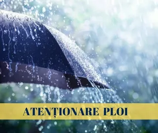 O umbrelă neagră este acoperită de picături de apă sub o ploaie intensă într-un decor cu fundal verde blurat.