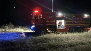 Un autospecial de pompieri roșu cu marcajul POMPIERII este parcat pe un teren cu iarbă uscată sub lumină nocturnă.