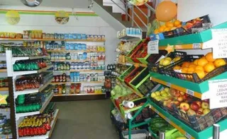 Rafturile unui magazin sunt umplute cu diverse produse alimentare, inclusiv fructe și legume așezate în coșuri pe suporturi de culoare verde.