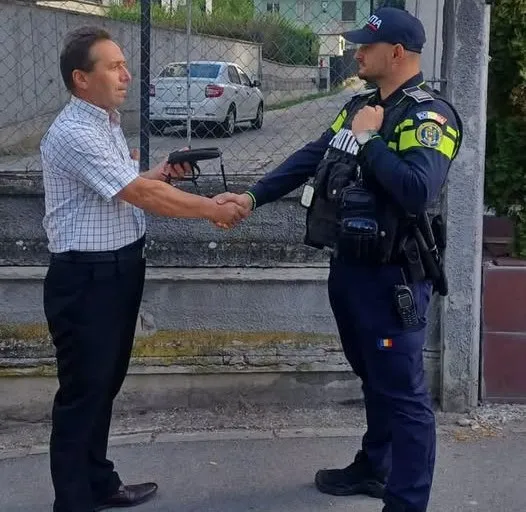 Un bărbat într-un cămașă tip cuadros și pantaloni închiși dă mâna unui polițist care poartă uniformă albastră și echipament tactic.