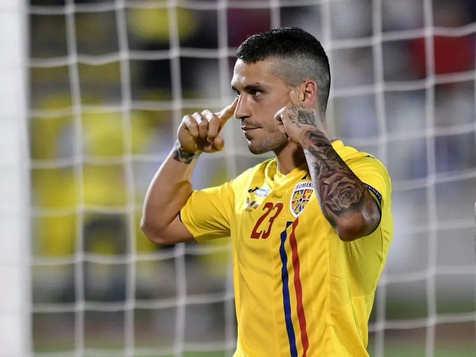 Un bărbat cu tricou galben numărul 23 își atinge obrajii cu degetele arătătoare în fața unei plase de fotbal.