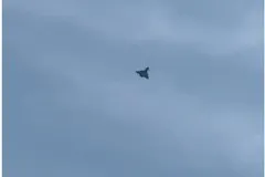 O siluetă întunecată de avion zboară pe un cer acoperit de nori gri.