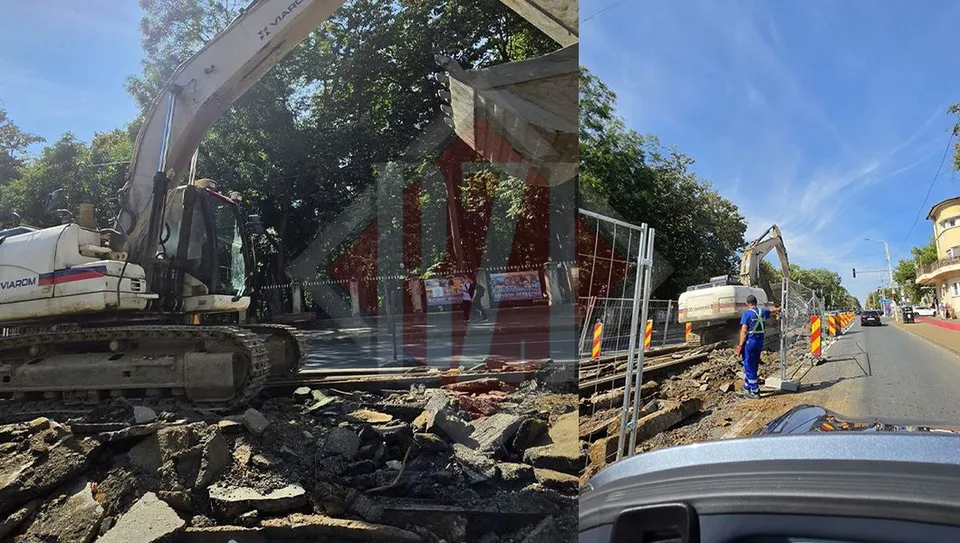 O excavatoare albă stă pe un teren cu resturi de asfalt lângă un gard metalic și un drum asfaltat sub un cer senin.