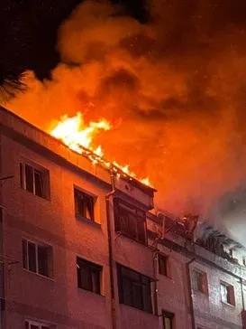 Flăcări mari și fum dens ies de pe acoperișul unei clădiri de locuințe pe timp de noapte.