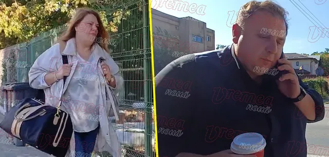 O femeie cu o geantă mare merge pe lângă un gard, în timp ce un bărbat vorbește la telefon lângă o clădire.