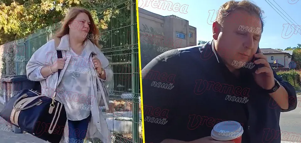 O femeie cu o geantă mare merge pe lângă un gard, în timp ce un bărbat vorbește la telefon lângă o clădire.