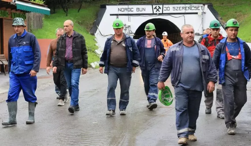 Un grup de bărbați îmbrăcați în haine de lucru și caschetă merge pe un drum umed.