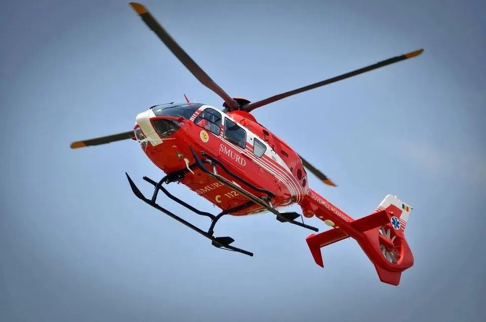 Un elicopter roșu cu inscripția SMURD zboară pe un cer gri.