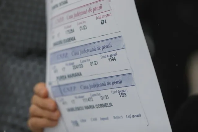O persoană ține o foaie de hârtie pe care sunt imprimate mai multe tabele cu text și cifre.