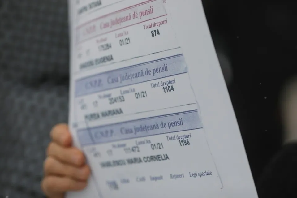 O persoană ține o foaie de hârtie pe care sunt imprimate mai multe tabele cu text și cifre.