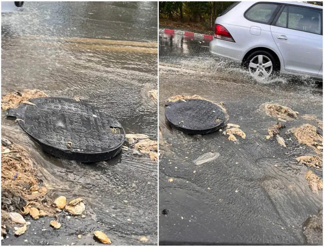 Un capac de canalizare negru este întins pe asfaltul acoperit de apă, lângă resturi de țărână și un autoturism argintiu.