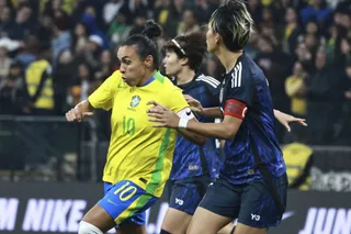 O jucătoare de fotbal în echipament galben și albastru este încadrată între două jucătoare în echipament închis în timpul unui meci.
