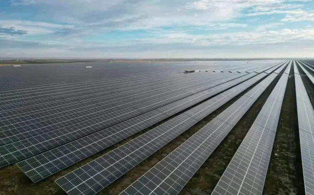 Rânduri lungi de panouri solare sunt dispuse pe un teren deschis sub un cer cu nori difuși.