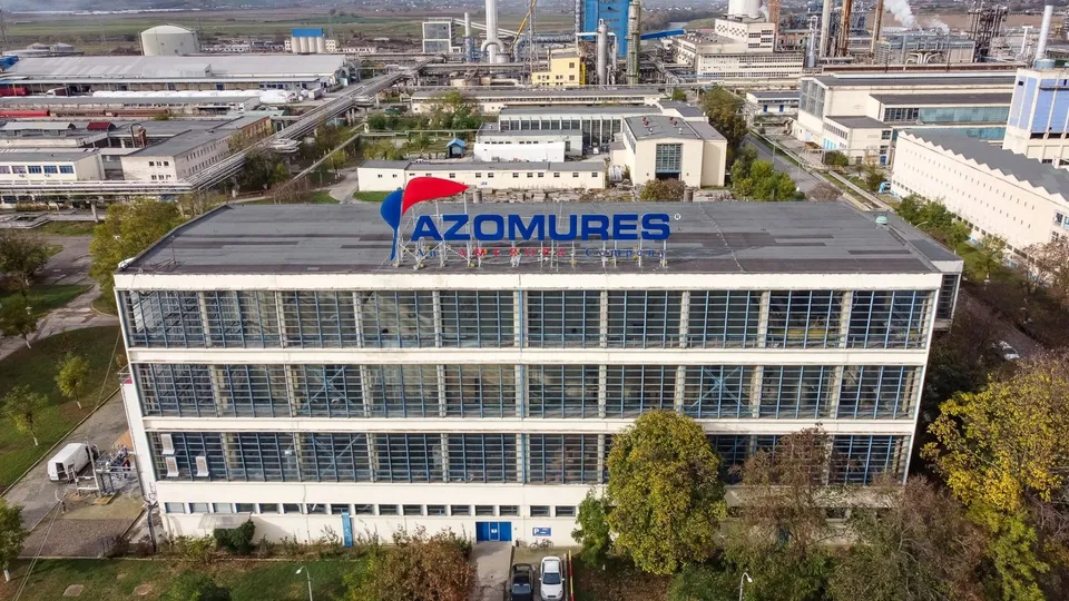 O vedere aeriană a unui clădire de birouri cu un semn albastru pe acoperiș, înconjurată de alte structuri industriale și vegetație.