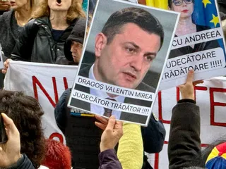 O persoană ține un poster cu portretul unui bărbat și text scris pe fundal alb.