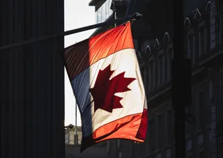 O steag al Canadei fluturând în vânt, înainte de o clădire urbană cu arhitectură clasică.