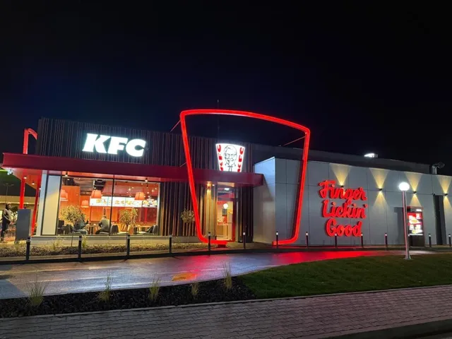 O clădire de tip restaurant cu iluminare roșie, afișajul KFC și inscripția Finger Lickin' Good sub un cer nocturn.
