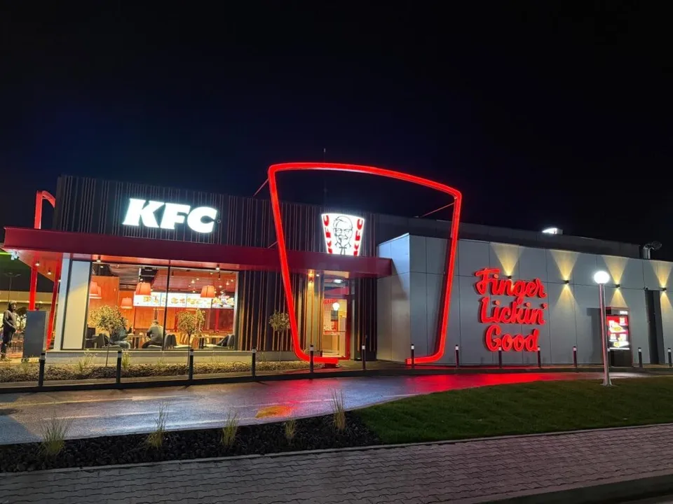 O clădire de tip restaurant cu iluminare roșie, afișajul KFC și inscripția Finger Lickin' Good sub un cer nocturn.