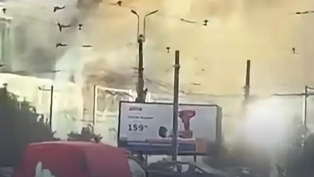 Fum dens și alb se ridică deasupra unor structuri și un panou publicitar situat lângă un stâlp de iluminat public.