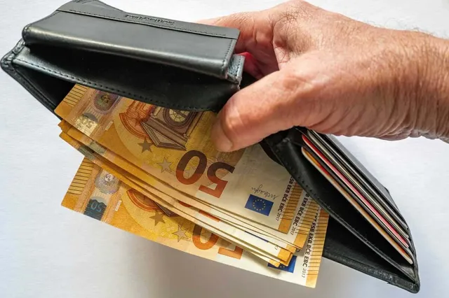 O mână ține un portofel deschis care conține mai multe bancnote de cincizeci de euro.