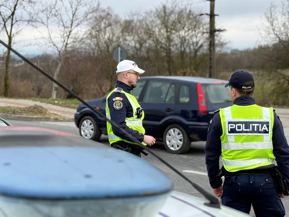 Un polițist cu vestă reflectorizantă și șapcă albă stă lângă o autoutilitară, în timp ce un alt polițist cu vestă reflectorizantă este văzut din spate.