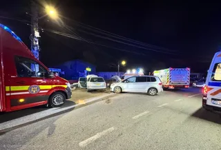 Două ambulanțe și mai multe autoturisme sunt parcate pe un drum asfaltat sub iluminat nocturn.