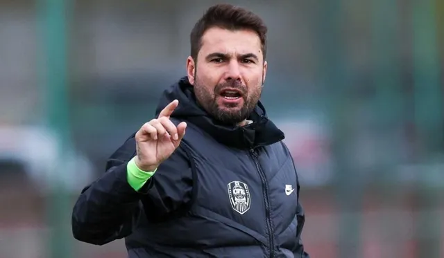 Fostul fotbalist Adrian Mutu, îmbrăcat într-o vestă neagră, vorbește și indică în timpul unei activități pe un teren sportiv.