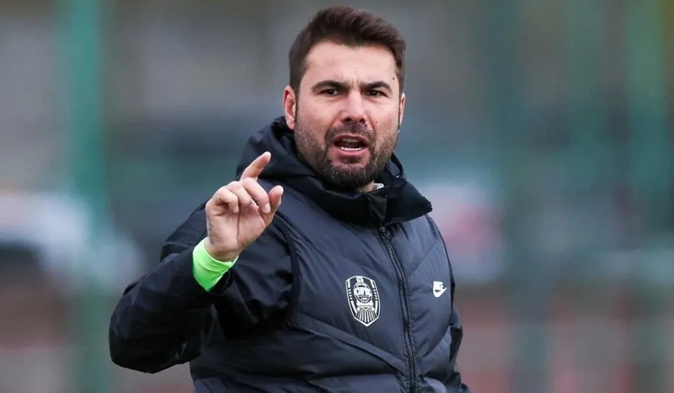 Fostul fotbalist Adrian Mutu, îmbrăcat într-o vestă neagră, vorbește și indică în timpul unei activități pe un teren sportiv.